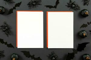 Blank greeting cards mockup and red envelopes on dark black background with pumpkins, spiders and bats. Halloween flat lay composition concept. Top view. Copy space. photo