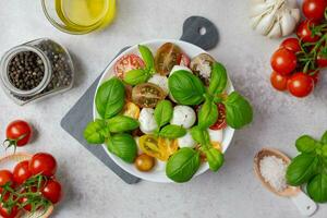 tradicional italiano caprese ensalada con Cereza Tomates, queso Mozzarella, albahaca, aceituna aceite, especias y mar sal. orgánico y natural comida concepto. ligero antecedentes. parte superior vista. foto