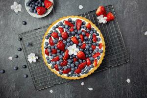 Delicious blueberry and strawberry tart with whipped cream and mascarpone on a dark stone background. Top view. photo