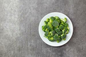 Raw broccoli on a white plate on a dark gray concrete background. Top view. Copy space. photo