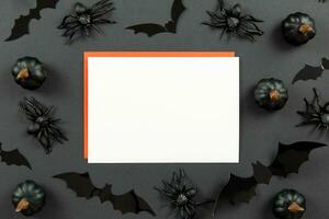 Blank greeting card mockup and red envelopes on dark black background with pumpkins, spiders and bats. Halloween flat lay composition concept. Top view. Copy space. photo