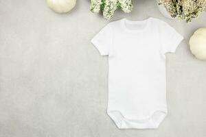White baby girl or boy bodysuit mockup flat lay with pumpkins on gray concrete background. Design onesie template, print presentation mock up. Top view. photo