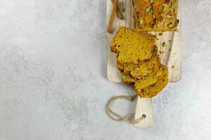 Pumpkin bread, cake on a wooden cutting board with pecan nuts, pumpkin seeds and cinnamon spices on a light gray background. Top view. Copy space. photo