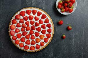 Delicious strawberry tart with whipped cream and mascarpone on a dark concrete background. Top view. photo
