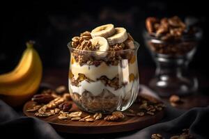 Yogurt granola parfait with sliced nuts and fresh banana fruits in a glass jar on dark background. . photo