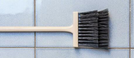 Photo of a white brush against a vibrant blue tiled wall with empty space for copy with copy space