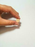 Isolated white photo of a hand holding a brown medicine tablet.