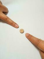 Isolated white photo of two forefingers pointing at a brown medicine tablet.