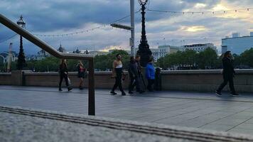 hermosa bajo ángulo imágenes de turista personas son caminando a lo largo ruta de Londres ojo a Westminster central Londres ciudad de Inglaterra genial Bretaña, imágenes estaba capturado en ago 02, 2023 durante puesta de sol. video