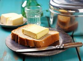 Foil wrapped processed cream cheese, table knife and slice of bread on a cutting board over blue wooden table. Small triangular pieces of soft cheese. Created with Generative AI technology. photo