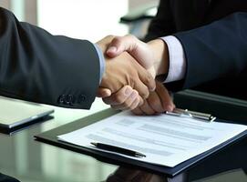 Close up of two businessmen shaking hands in blurred office with computer and contract on table. Concept of partnership and communication Created with Generative AI technology. photo