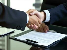 Close up of two businessmen shaking hands in blurred office with computer and contract on table. Concept of partnership and communication Created with Generative AI technology. photo