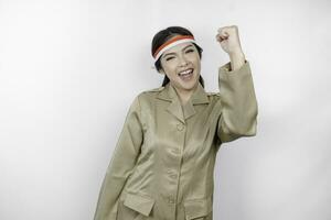 A young Asian government worker with a happy successful expression, wearing flag headband and khaki uniform isolated by white background. Indonesia's independence day concept. photo