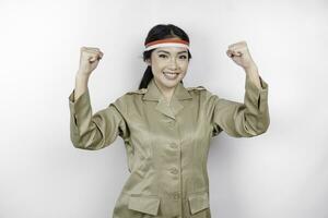 A young Asian government worker with a happy successful expression, wearing flag headband and khaki uniform isolated by white background. Indonesia's independence day concept. photo