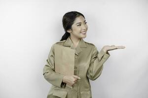 A Young beautiful Asian worker with brown uniform bringing document and pointing to copy space beside her. Indonesian PNS. photo