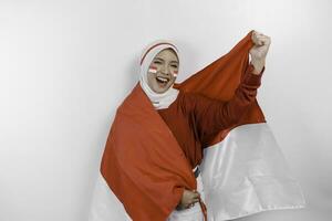 un joven asiático musulmán mujer con un contento exitoso expresión vistiendo rojo parte superior y blanco hijab mientras participación de indonesia bandera, aislado por blanco antecedentes. de indonesia independencia día concepto. foto