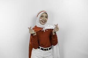 Happy smiling Indonesian muslim woman holding Indonesia's flag and showing love sign to celebrate Indonesia Independence Day isolated over white background. photo