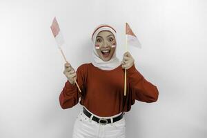 un joven asiático musulmán mujer con un contento exitoso expresión vistiendo rojo parte superior y blanco hijab mientras participación de indonesia bandera, aislado por blanco antecedentes. de indonesia independencia día concepto. foto