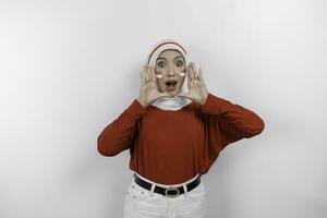 Young beautiful muslim woman wearing a red top and white hijab is shouting and screaming loud with a hand on her mouth. Indonesia's independence day concept. photo