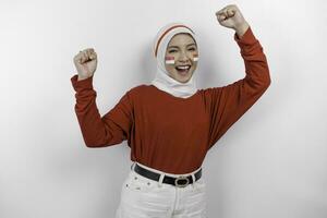 A young Asian muslim woman with a happy successful expression wearing red top and white hijab isolated by white background. Indonesia's independence day concept. photo