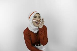joven hermosa musulmán mujer vistiendo un rojo parte superior y blanco hijab es gritos y gritando ruidoso con un mano en su boca. de indonesia independencia día concepto. foto