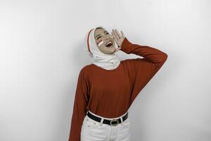 Young beautiful muslim woman wearing a red top and white hijab is shouting and screaming loud with a hand on her mouth. Indonesia's independence day concept. photo