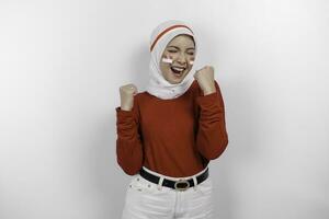 A young Asian muslim woman with a happy successful expression wearing red top and white hijab isolated by white background. Indonesia's independence day concept. photo