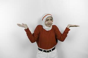 A thoughtful young muslim woman wearing white hijab and red top is confuse between choices beside her, isolated by white background. Indonesia's independence day. photo