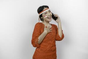 contento consciente de agradecido joven asiático mujer vistiendo rojo kebaya y participación teléfono y mano en cofre sonriente aislado en blanco antecedentes sensación No estrés, foto
