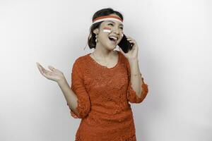 un contento asiático mujer vistiendo rojo kebaya y venda, participación su teléfono, y señalando Copiar espacio junto a su, aislado por blanco antecedentes. de indonesia independencia día foto