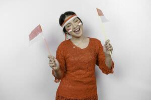 Happy smiling Indonesian woman wearing red kebaya and headband holding Indonesia's flag to celebrate Indonesia Independence Day isolated over white background. photo