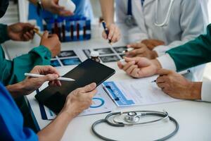 Medical team having a meeting with doctors in white lab coats and surgical scrubs seated at a table discussing a patients working online using computers in the medical industry photo