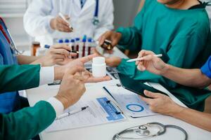Medical team having a meeting with doctors in white lab coats and surgical scrubs seated at a table discussing a patients working online using computers in the medical industry photo