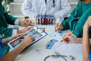 Medical team having a meeting with doctors in white lab coats and surgical scrubs seated at a table discussing a patients working online using computers in the medical industry photo