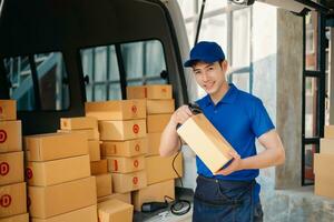 sonriente entrega hombre en pie en frente de su camioneta con participación caja y tableta entrega hogar y Envío foto