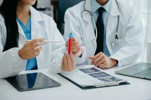 Medical team having a meeting with doctors in white lab coats and surgical scrubs seated at a table discussing a patients working online using computers in the medical industry photo