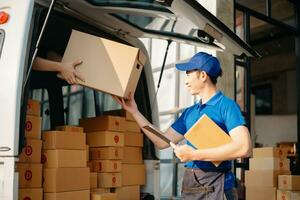 Smiling delivery man standing in front of his van with Holding Box and tablet delivery home and shipping photo