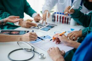 Medical team having a meeting with doctors in white lab coats and surgical scrubs seated at a table discussing a patients working online using computers in the medical industry photo