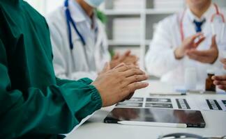 Medical team having a meeting with doctors in white lab coats and surgical scrubs seated at a table discussing a patients working online using computers in the medical industry photo