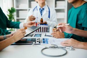 Medical team having a meeting with doctors in white lab coats and surgical scrubs seated at a table discussing a patients working online using computers in the medical industry photo