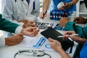 Medical team having a meeting with doctors in white lab coats and surgical scrubs seated at a table discussing a patients working online using computers in the medical industry photo