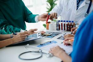 Medical team having a meeting with doctors in white lab coats and surgical scrubs seated at a table discussing a patients working online using computers in the medical industry photo