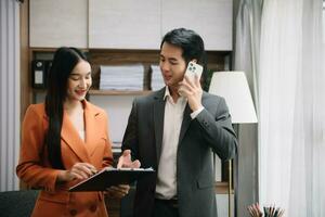 Asian business colleague business presents and explains and using laptop and tablet. Teamwork, financial marketing team,   while sitting in modern office photo
