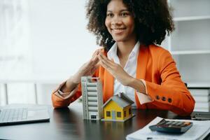 Female real estate agent is use hands to protect red roof for the concept of real estate investment about house trading, purchase at desk in office photo