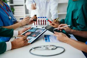 Medical team having a meeting with doctors in white lab coats and surgical scrubs seated at a table discussing a patients working online using computers in the medical industry photo