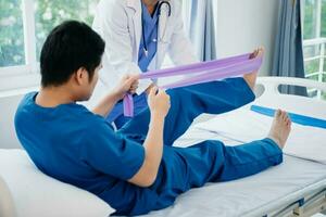 fisioterapeuta Ayudar paciente mientras extensión su pierna en cama en clínica foto