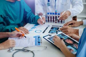 Medical team having a meeting with doctors in white lab coats and surgical scrubs seated at a table discussing a patients working online using computers in the medical industry photo