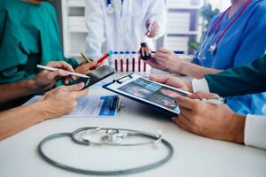 Medical team having a meeting with doctors in white lab coats and surgical scrubs seated at a table discussing a patients working online using computers in the medical industry photo