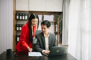 Asian business colleague business presents and explains and using laptop and tablet. Teamwork, financial marketing team,   while sitting in modern office photo