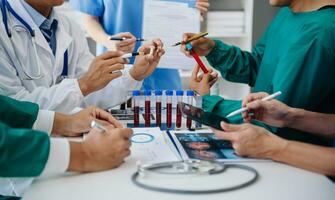 Medical team having a meeting with doctors in white lab coats and surgical scrubs seated at a table discussing a patients working online using computers in the medical industry photo